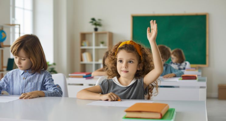 young girl raising her hand in a classroom setting
